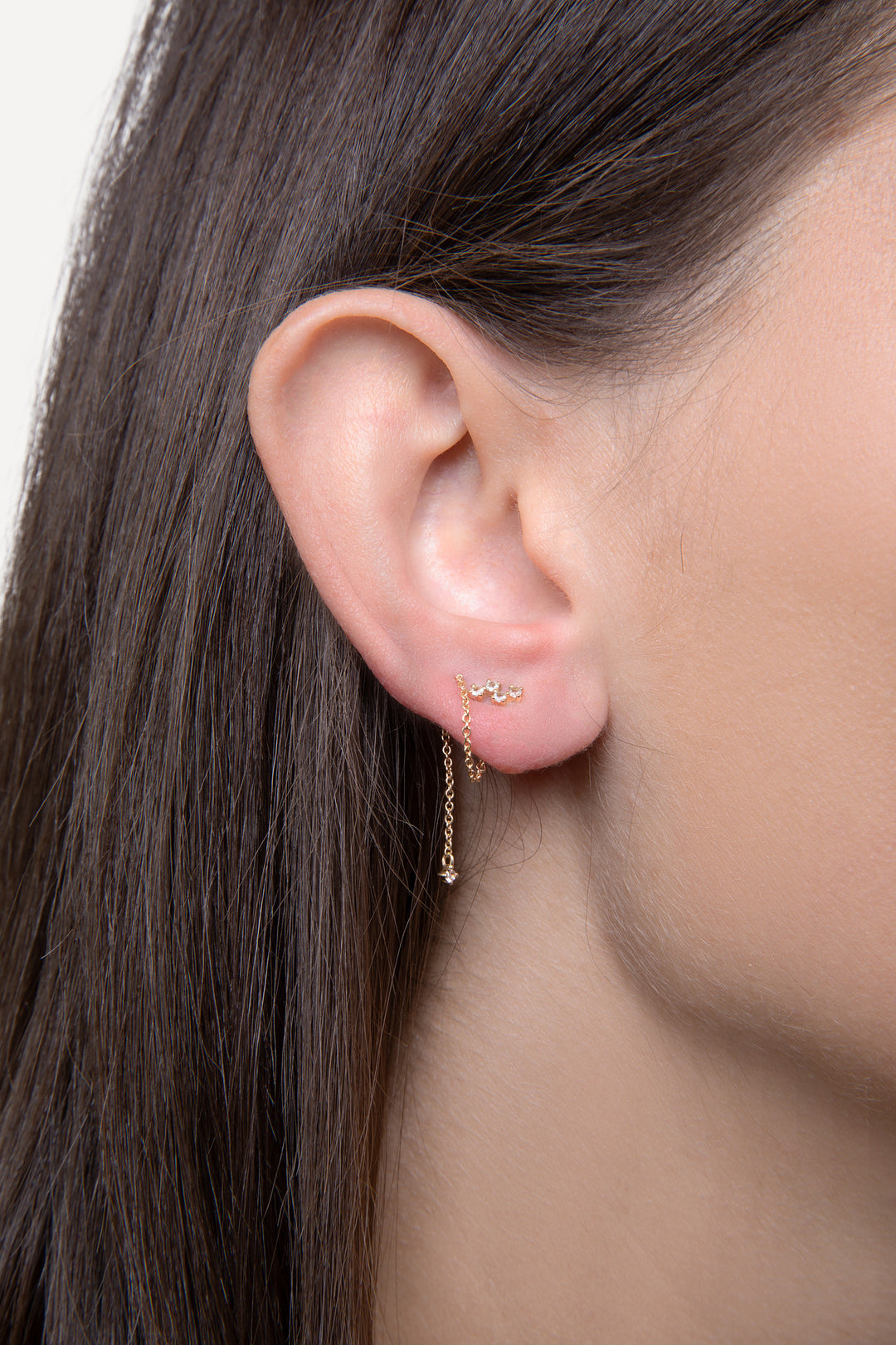 An image of a woman’s ear with two earrings. The warring is a dangling chain earring with diamond accents