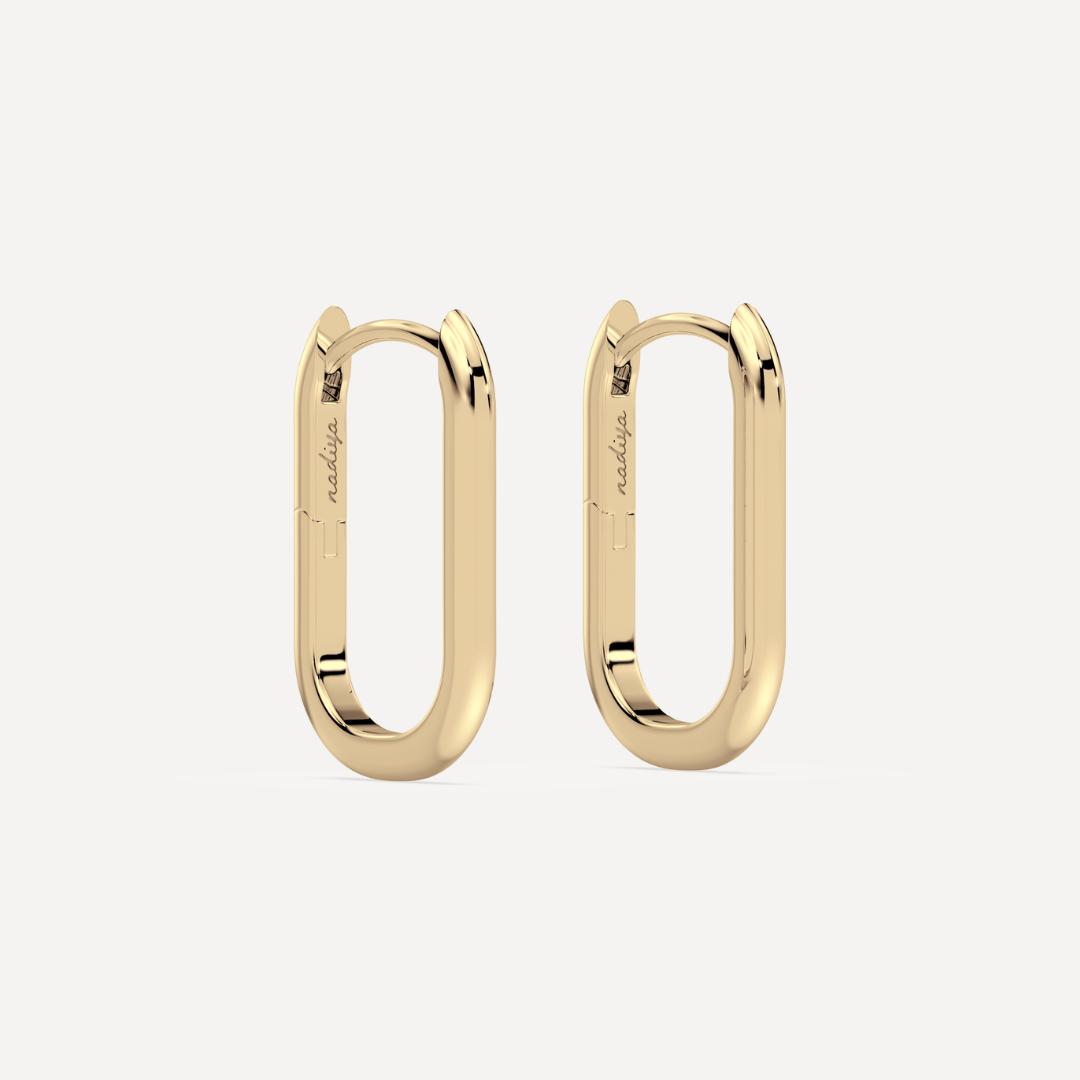 solid gold oval hoops against a creamy white background by nadiya jewelry