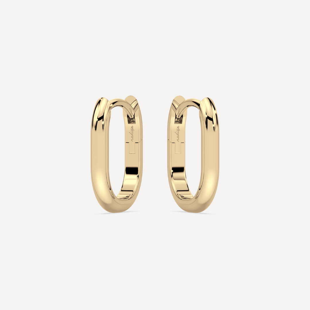 solid gold oval hoops against a creamy white background by nadiya jewelry