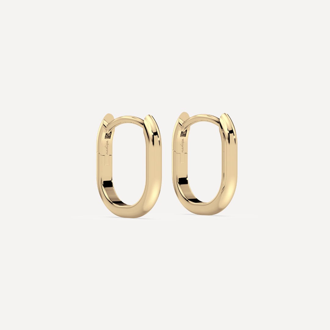 solid gold oval hoops against a creamy white background by nadiya jewelry
