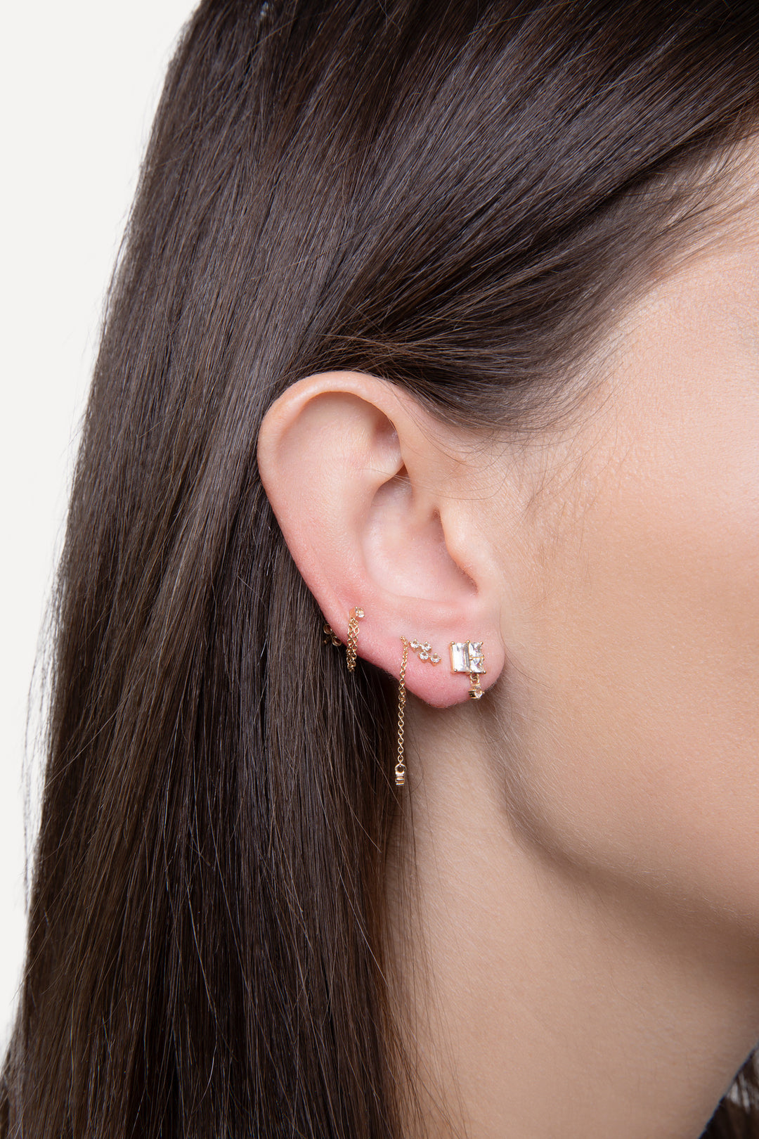 An image of a woman’s ear with three earrings. In solid gold and diamonds