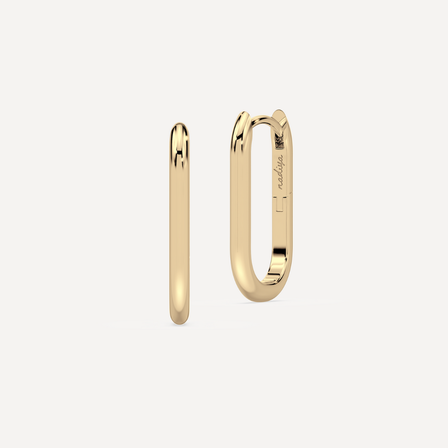 solid gold oval hoops against a creamy white background by nadiya jewelry