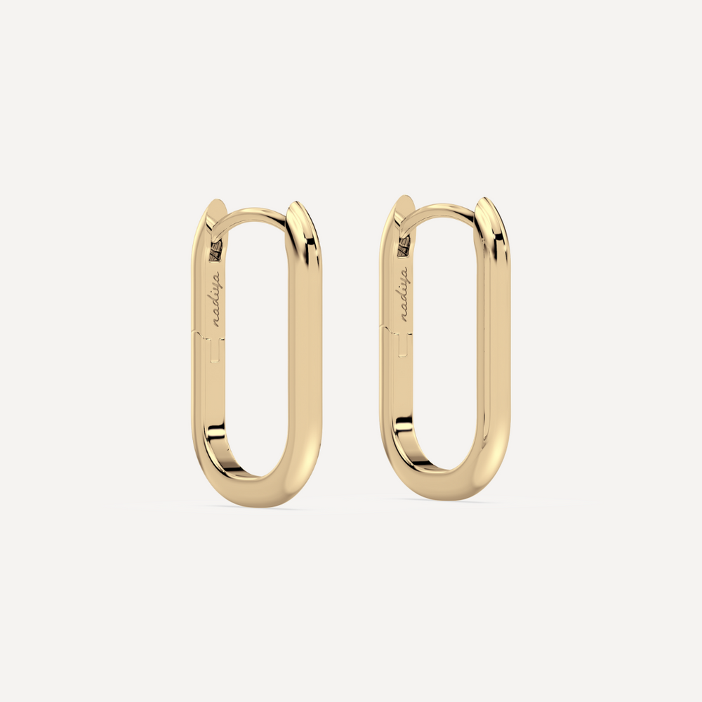 solid gold oval hoops against a creamy white background by nadiya jewelry