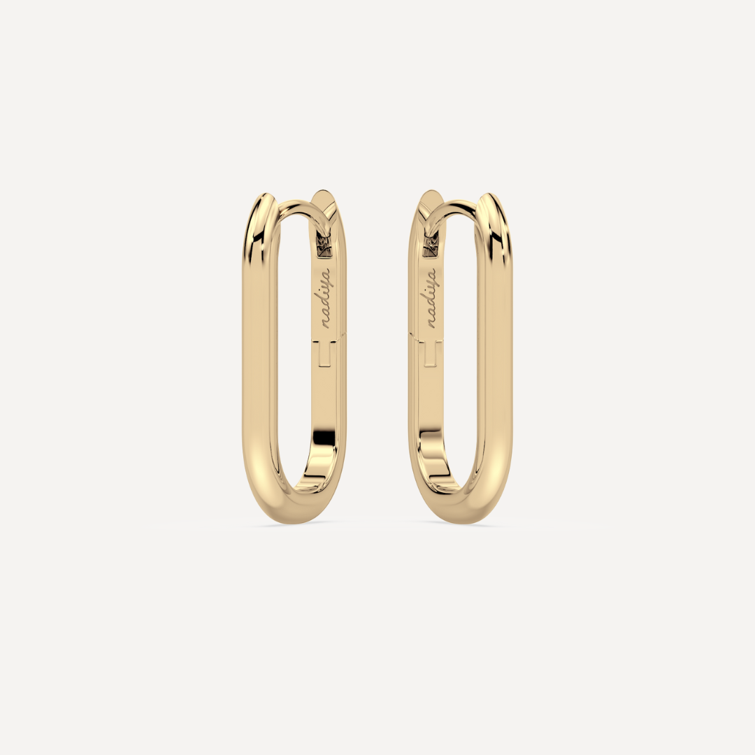 solid gold oval hoops on a creamy white background by nadiya jewelry