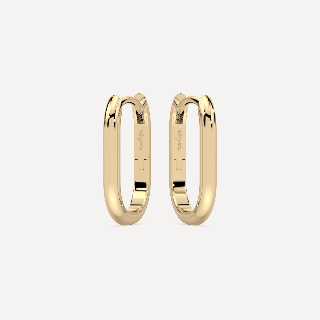 solid gold oval hoops against a creamy white background by nadiya jewelry