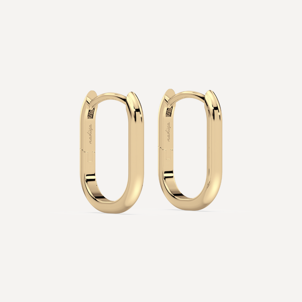solid gold oval hoops against a creamy white background by nadiya jewelry
