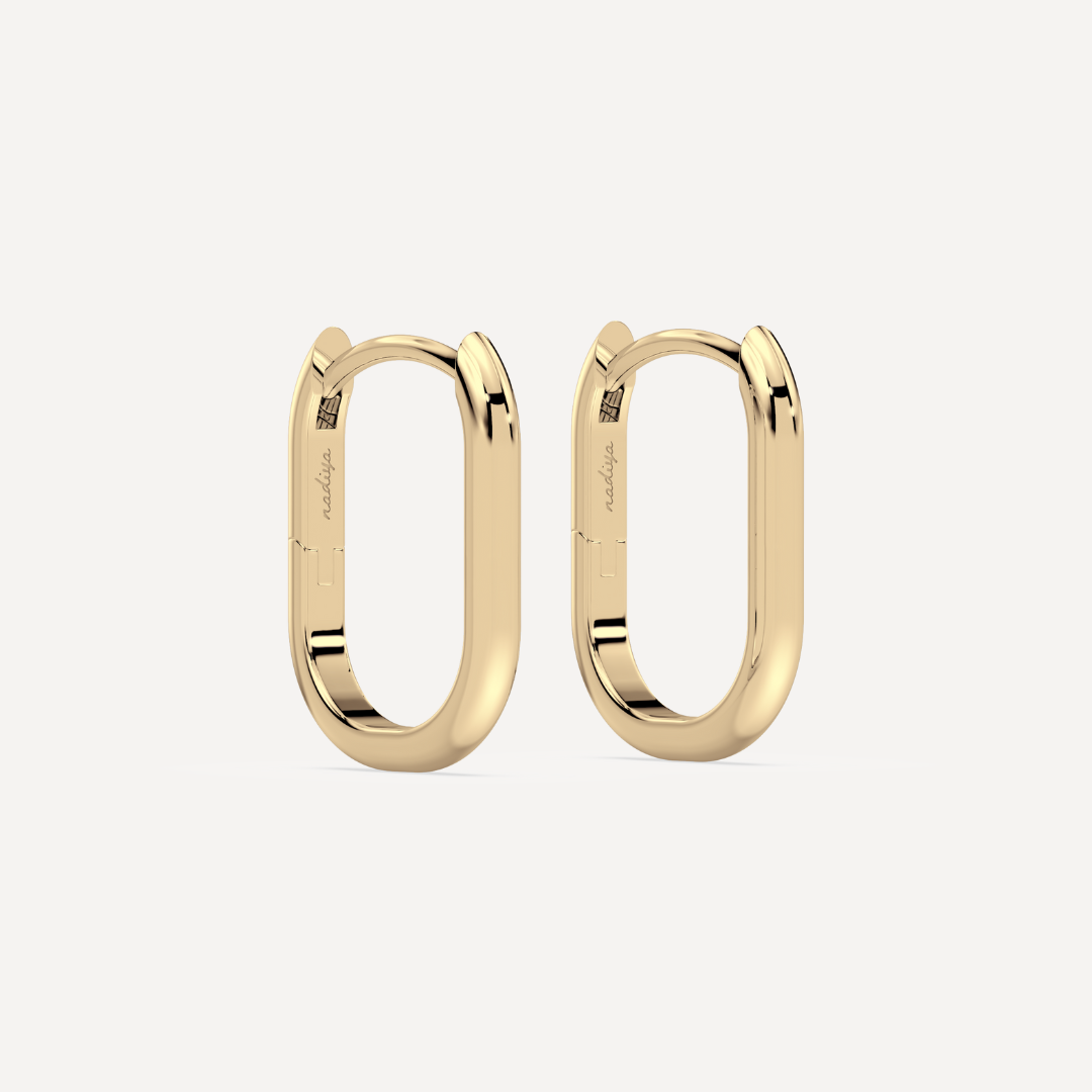 solid gold oval hoops against a creamy white background by nadiya jewelry
