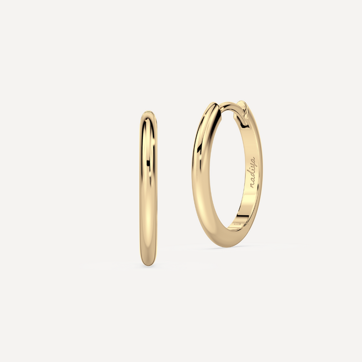 solid gold round hoops against a creamy white background by nadiya jewelry
