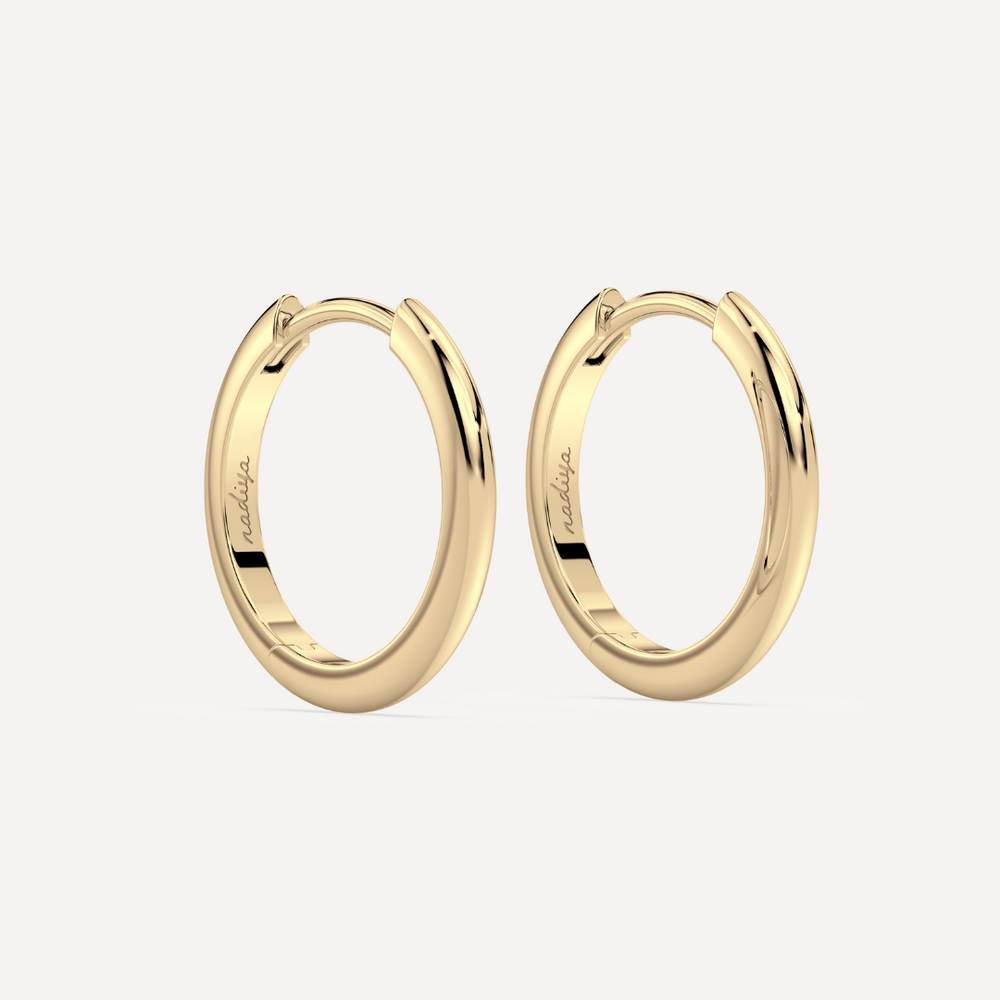 solid gold round hoops against a creamy white background by nadiya jewelry