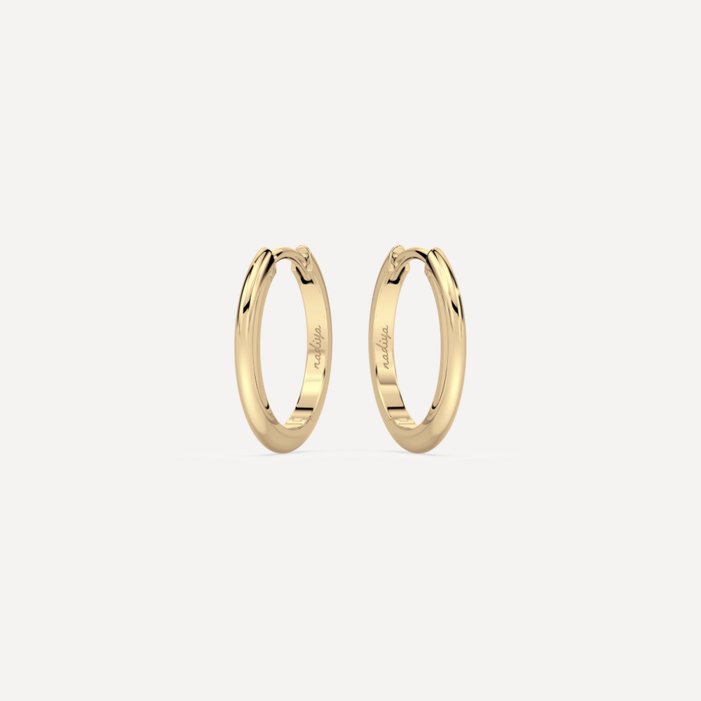 solid gold round hoops against a creamy white background by nadiya jewelry
