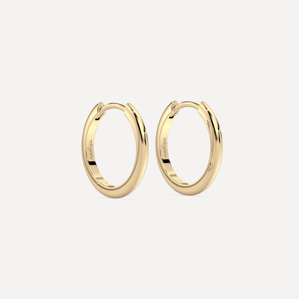 solid gold round hoops against a creamy white background by nadiya jewelry