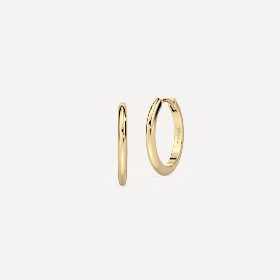 solid gold round hoops against a creamy white background by nadiya jewelry