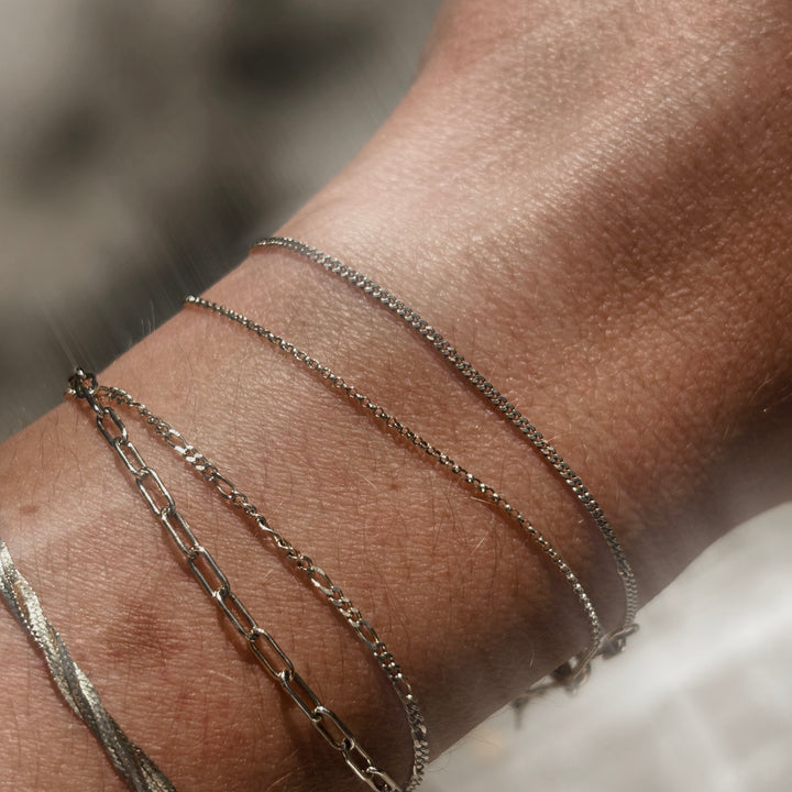 Close-up of a wrist wearing multiple solid gold chain bracelets on a blurred background